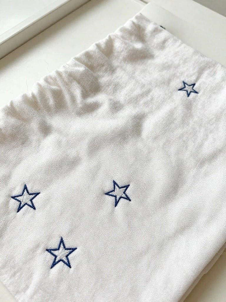 White pillowcase cuff with four small navy blue embroidered stars scattered along the edge.