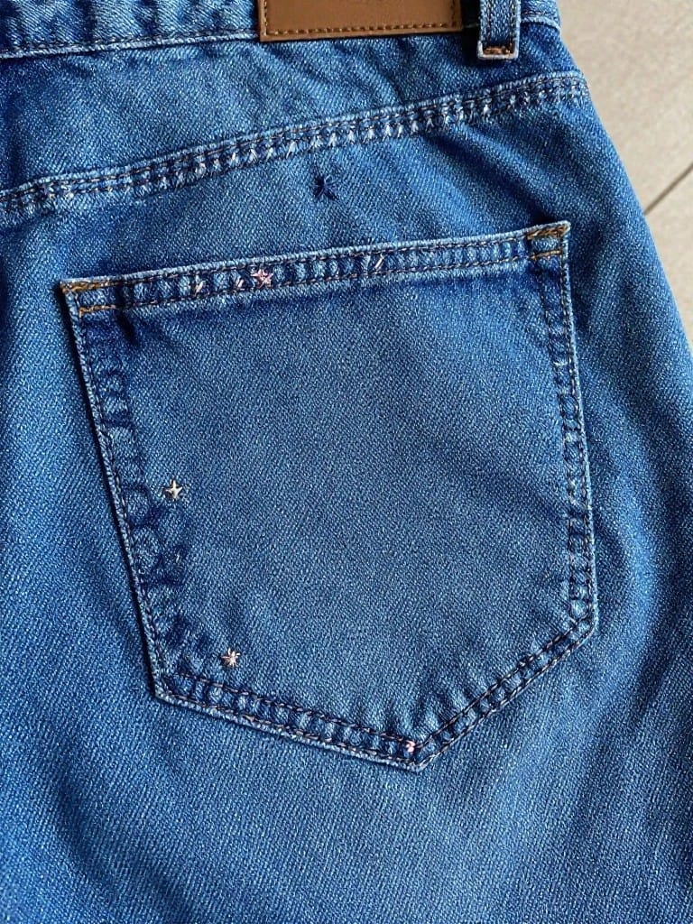 Blue jeans back pocket with small pink embroidered stars scattered along the upper edge and flap.