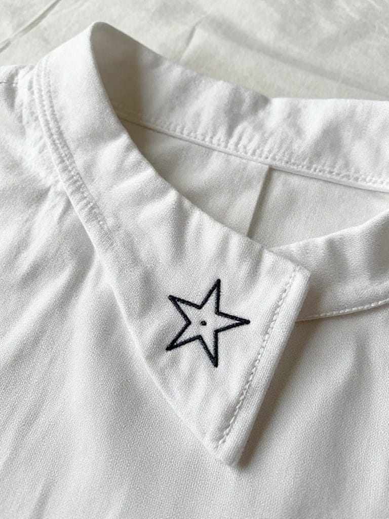 White shirt collar with a small black embroidered star on the pointed edge.