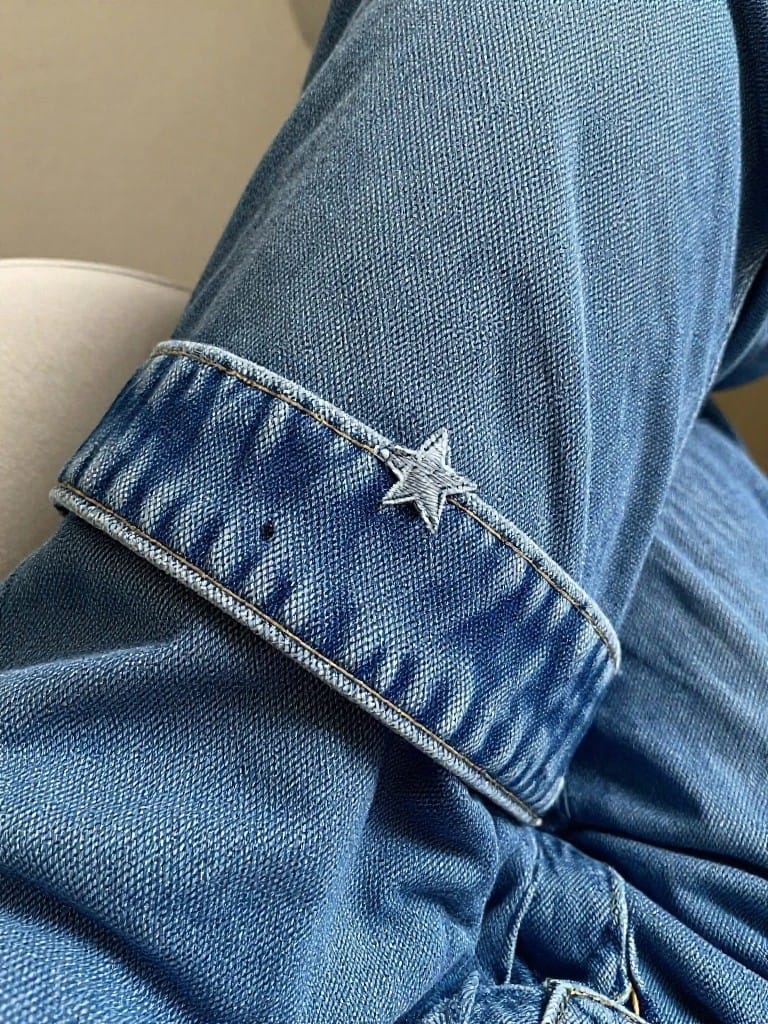 Close-up of a white embroidered star on the folded cuff of blue denim jeans.