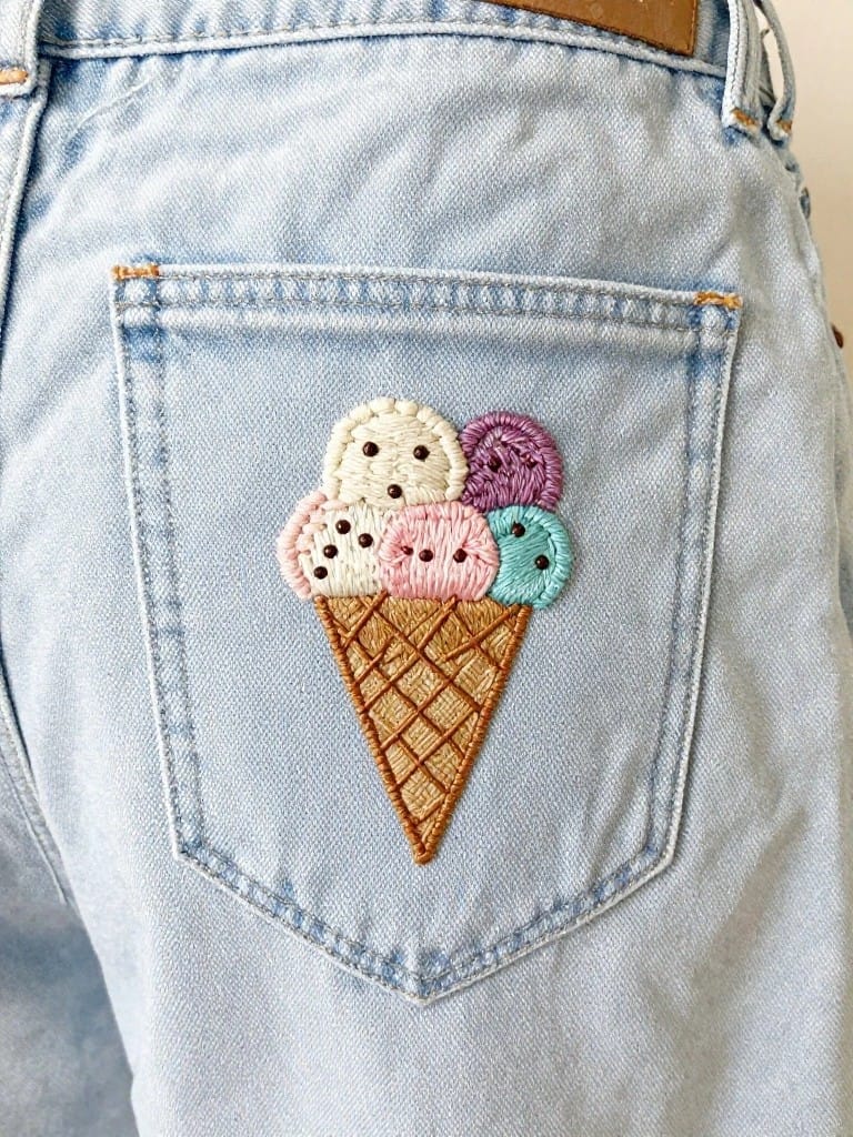 Light blue jeans with multicolored embroidered ice cream cone featuring button scoops on the back pocket.