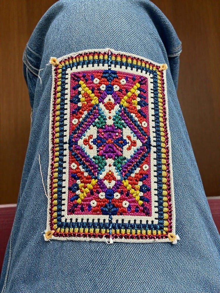 Colorful geometric embroidery patch sewn onto the back pocket of blue jeans.