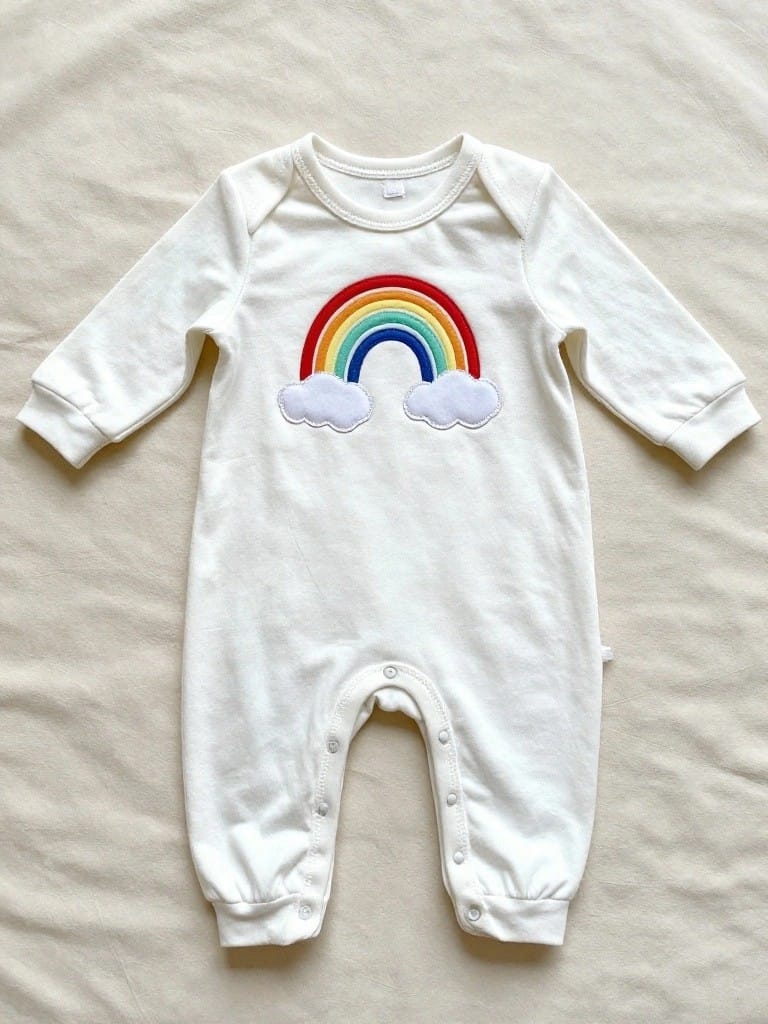 White long-sleeve baby onesie with colorful embroidered rainbow and white clouds on the chest.