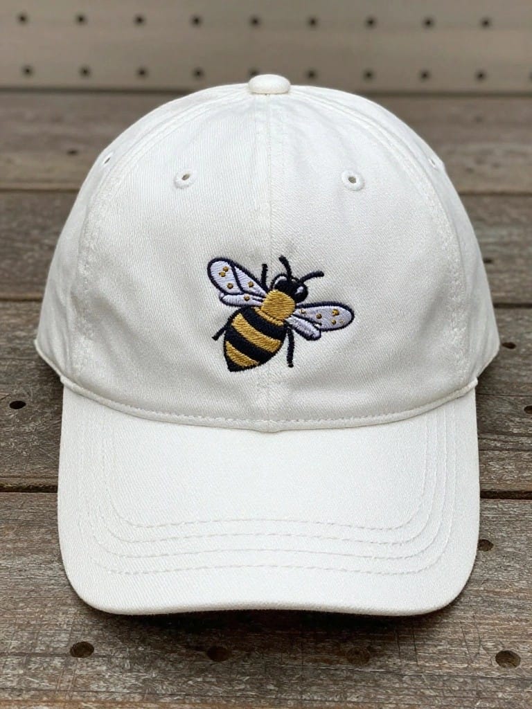 White baseball cap with yellow and black bumblebee embroidery on the front panel against a wooden surface.