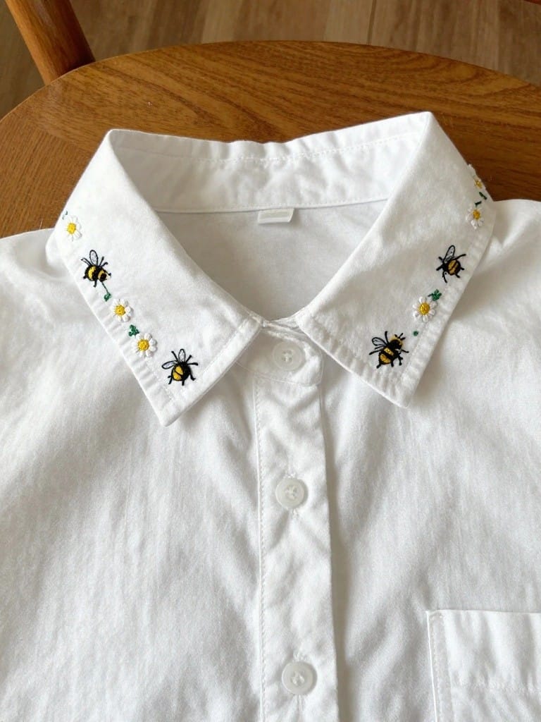 White shirt collar embroidered with yellow bees, white daisies, and green leaves along the edges.