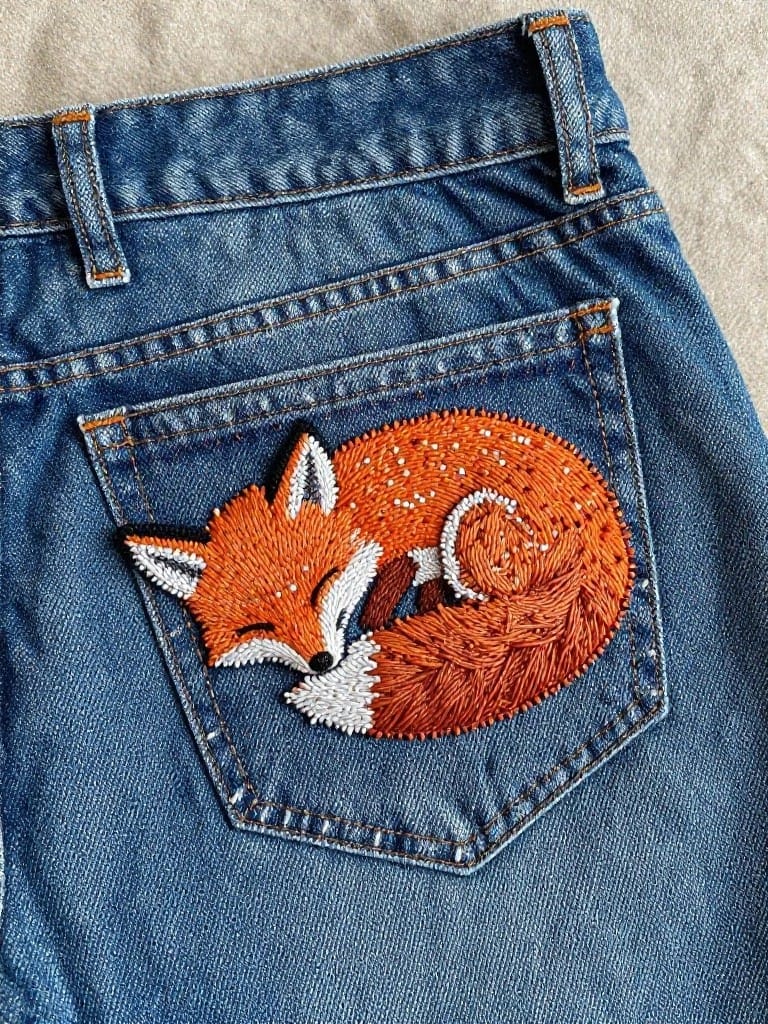 Embroidered orange fox curled up on the back pocket of blue jeans.