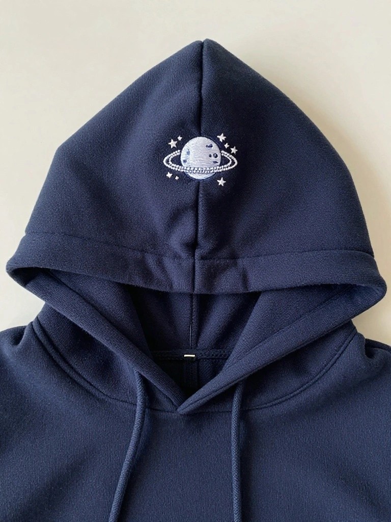 Navy blue hoodie hood embroidered with a white planet having rings and surrounding stars centered at the peak.