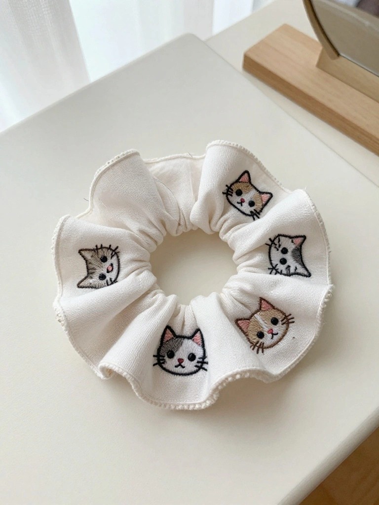 White ruffled scrunchie with five embroidered cat faces spaced around its edge.