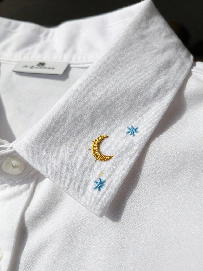 White collared shirt collar with gold embroidered crescent moon and two small blue embroidered stars on the flap.