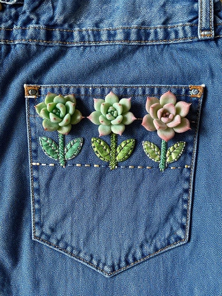 Three embroidered green and pink succulents with leaves on the flap of a blue denim pocket.