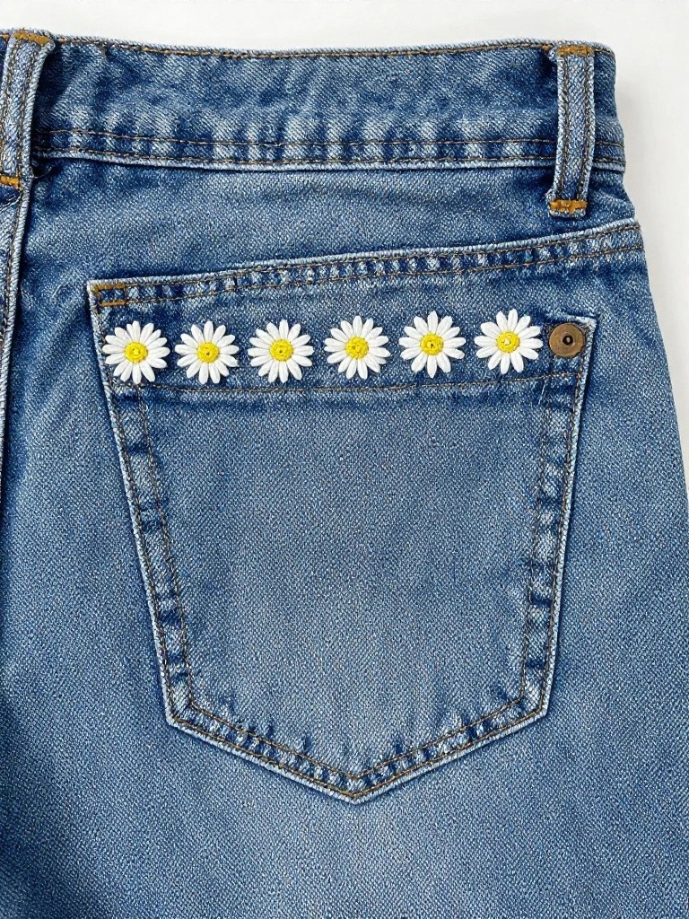 Jeans back pocket with a row of six small white daisies embroidered along the top edge.