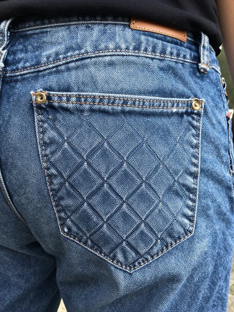 Back pocket of jeans embroidered with a diamond grid pattern and gold corner studs.