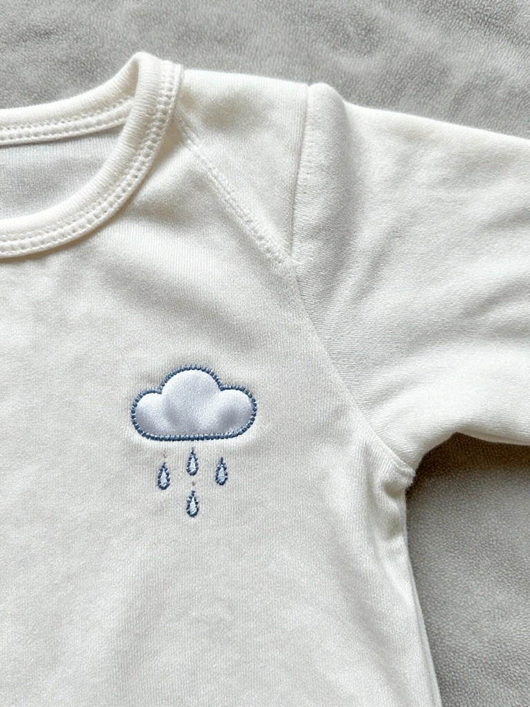 White baby onesie sleeve with blue embroidered cloud and three raindrops.
