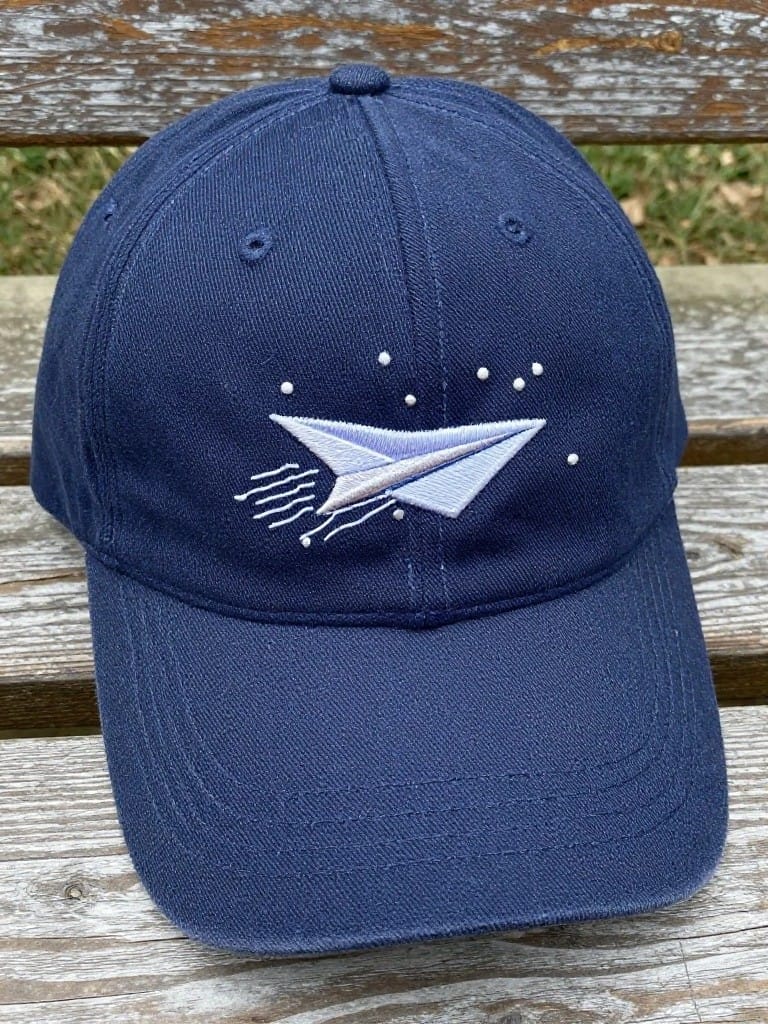 Navy baseball cap embroidered with a light blue paper airplane, white stars, and trailing lines on the front panel.