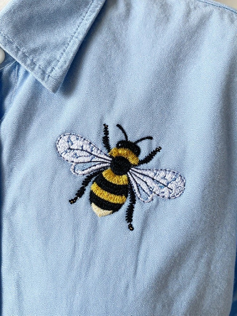 Light blue denim fabric with a centered embroidered bee featuring yellow-and-black stripes and white wings.