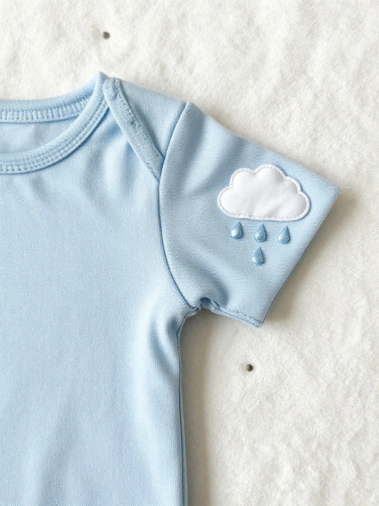 Light blue baby onesie laid flat with white embroidered cloud and blue raindrops on the short sleeve.