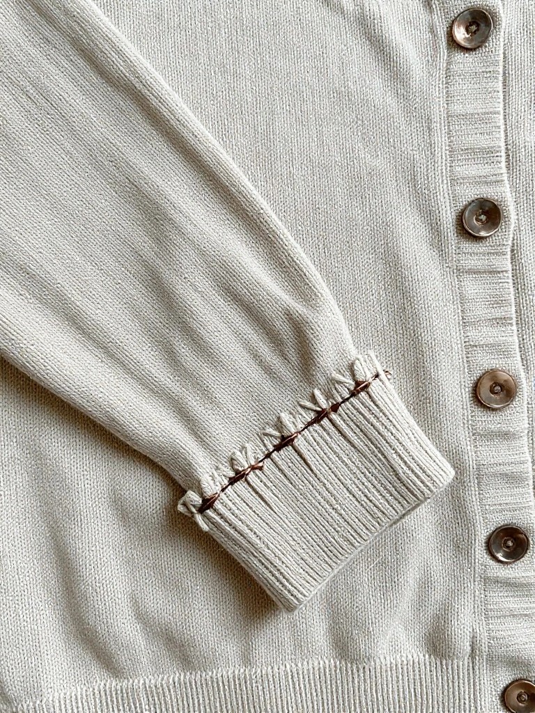 Close-up of cream knit cardigan sleeve cuffs outlined with darker thread in scalloped ruffles.
