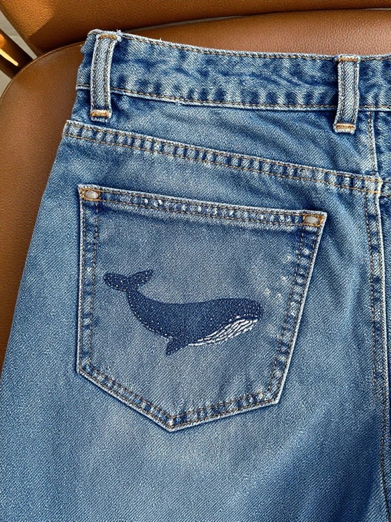 Back pocket of light-wash jeans with a small embroidered blue whale.