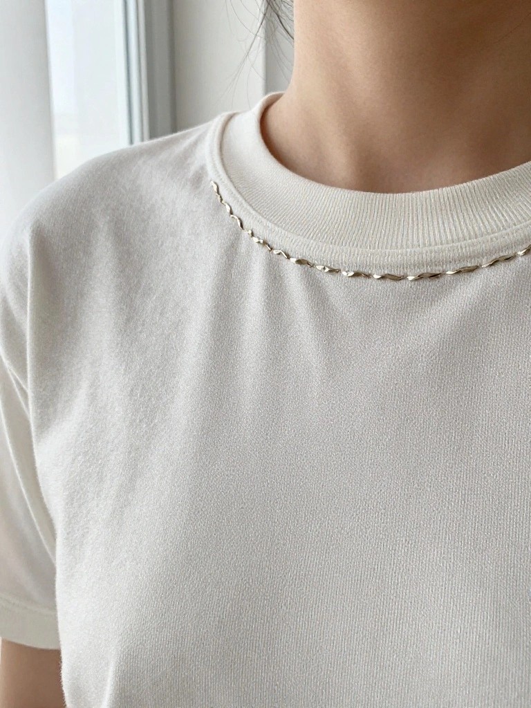 Close-up of a white crew neck t-shirt collar edged with thin silver chain-like embroidery.