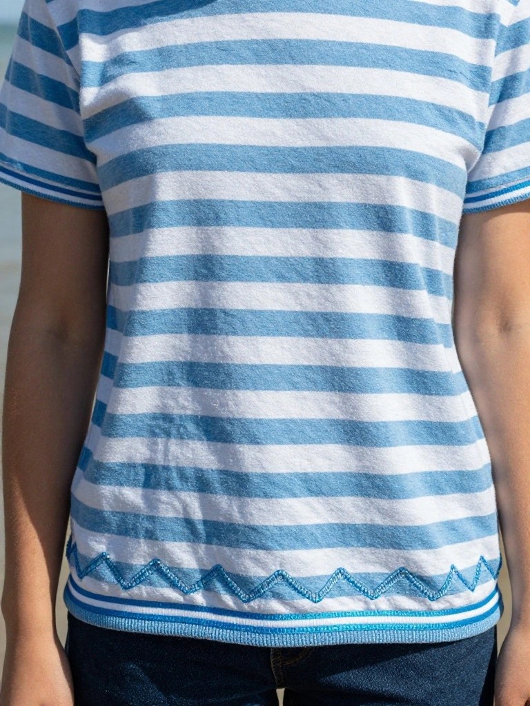 Close-up of a blue and white striped knit shirt with blue wavy scallop embroidery along the lower front hem.