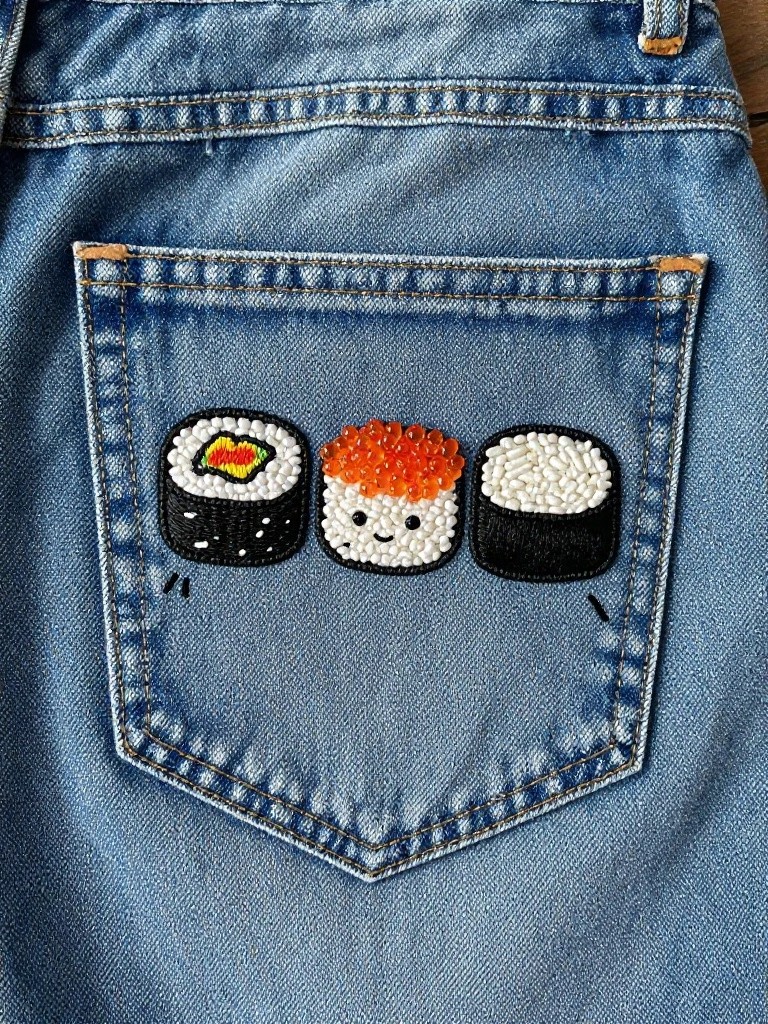 Blue jeans back pocket embroidered with three small sushi rolls that have faces.