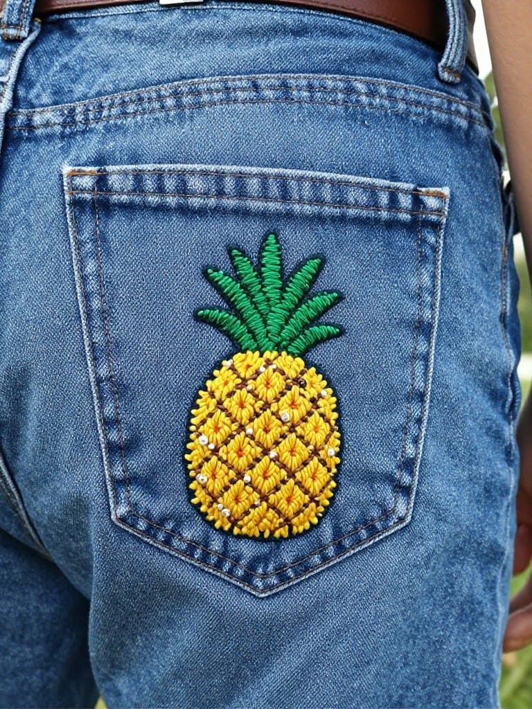 Blue jeans back pocket embroidered with a yellow pineapple and green leaves.