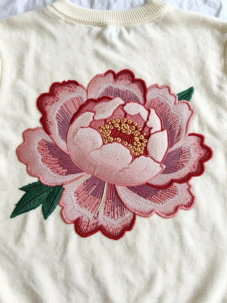 White knit sweater back with large embroidered pink peony flower and green leaves centered on the upper back.