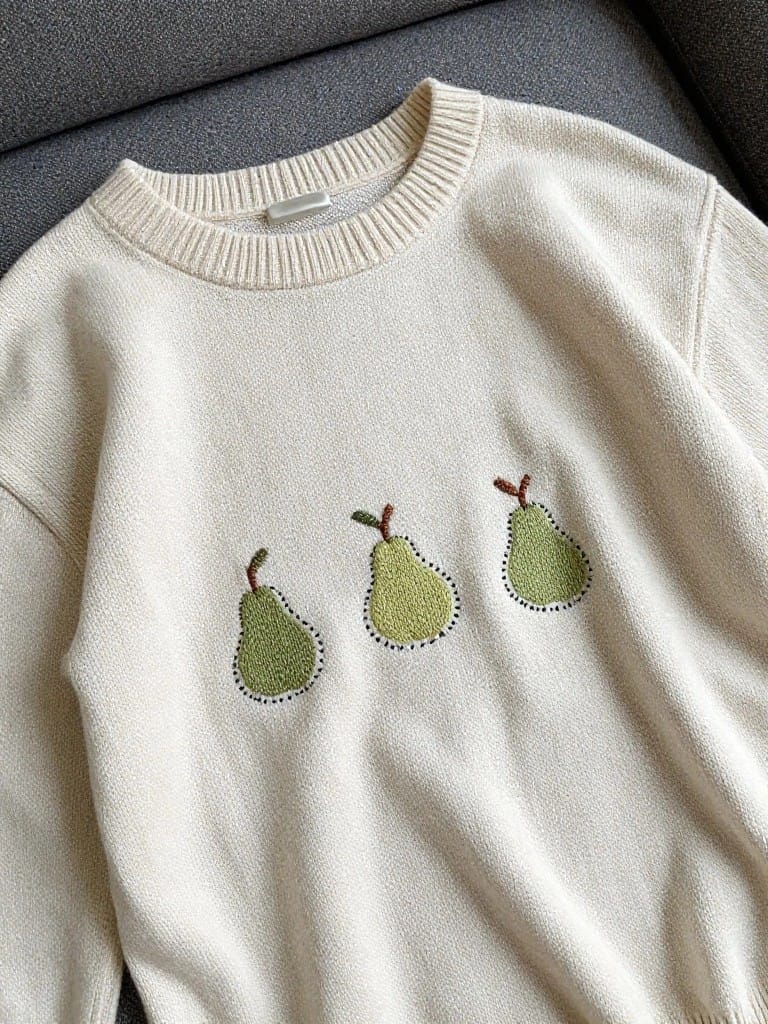 White knit sweater with three green embroidered pears and brown stems across the front chest.