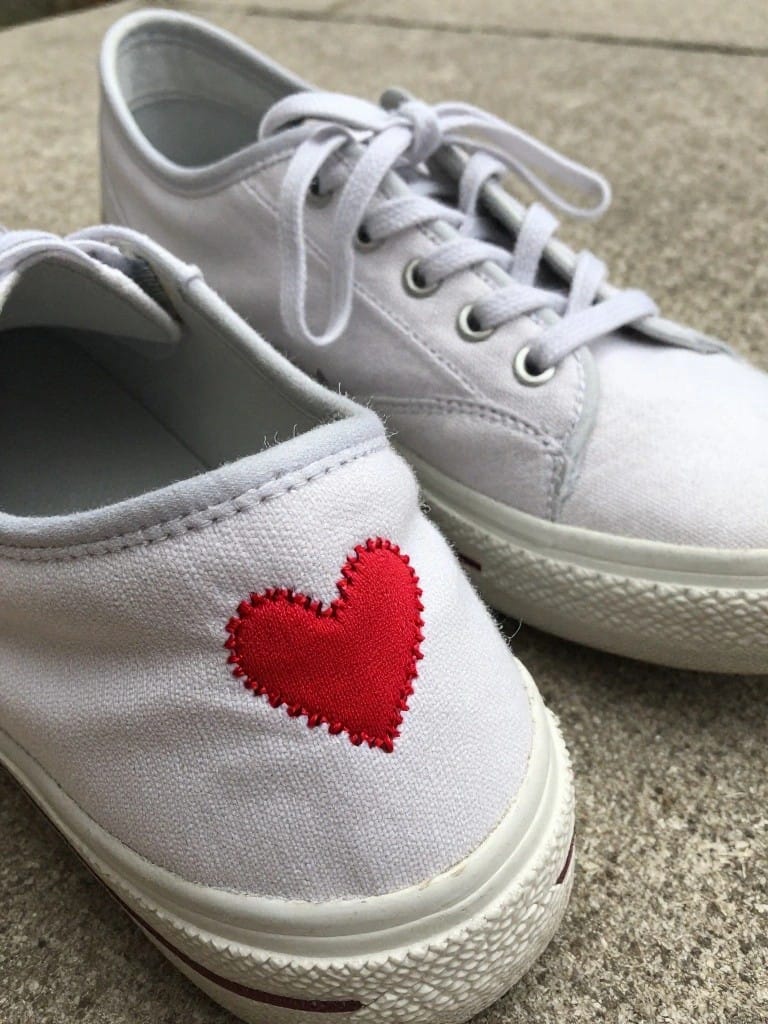 White canvas sneakers with a red embroidered heart on the outer side.