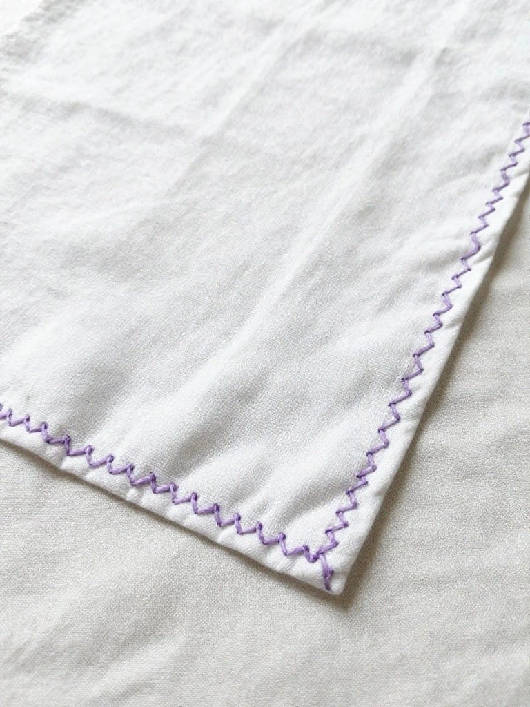 White rectangular napkin with purple zigzag running stitches along the edges.