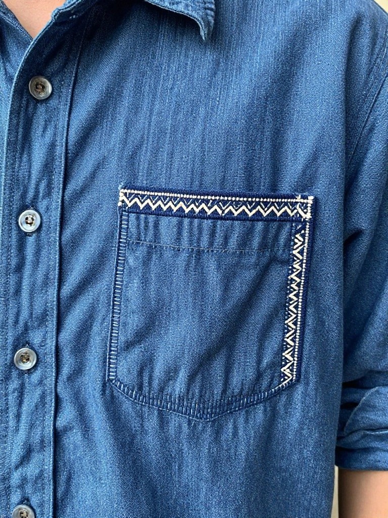 Close-up of a blue denim shirt pocket edged with white zigzag embroidery.