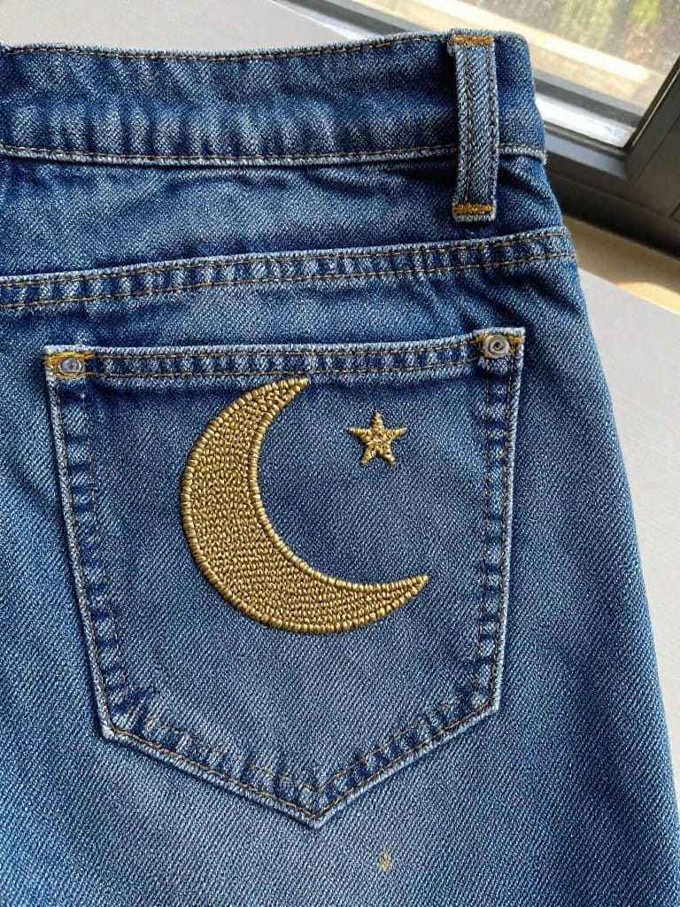 Gold embroidered crescent moon and star on the back pocket flap of blue jeans.