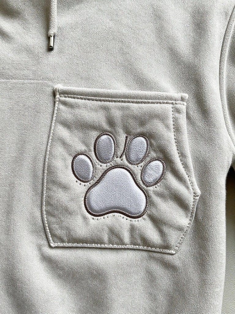 Light gray hoodie pocket with embroidered paw print in matching light tones.