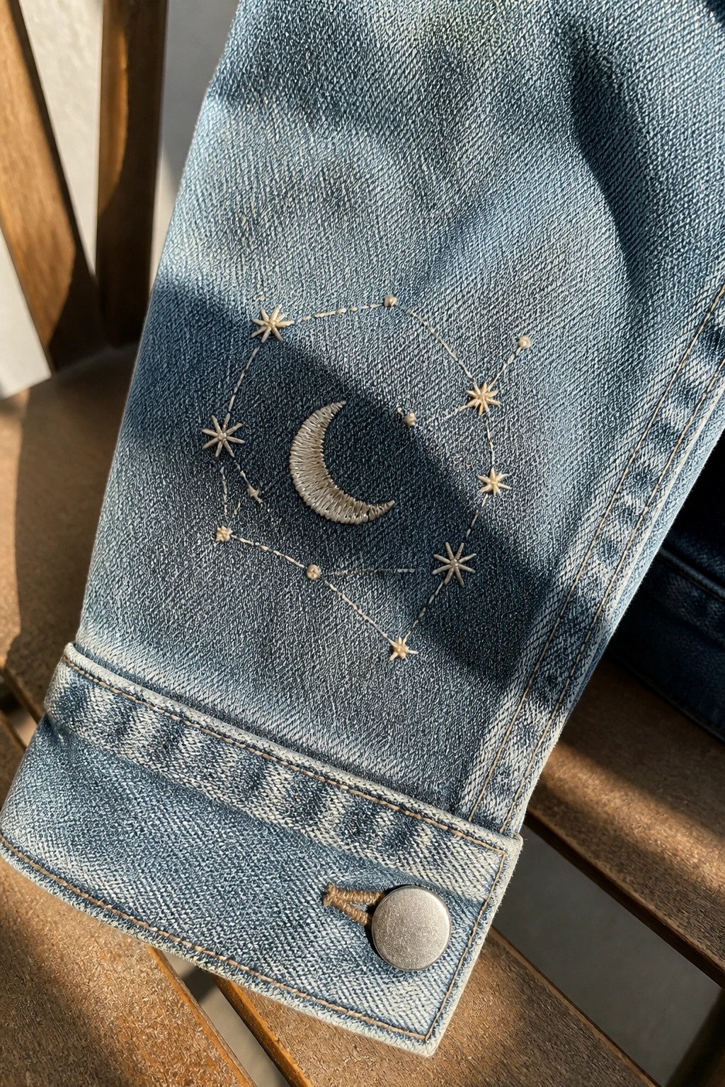 Light-wash denim jacket cuff with embroidered crescent moon and constellation stars