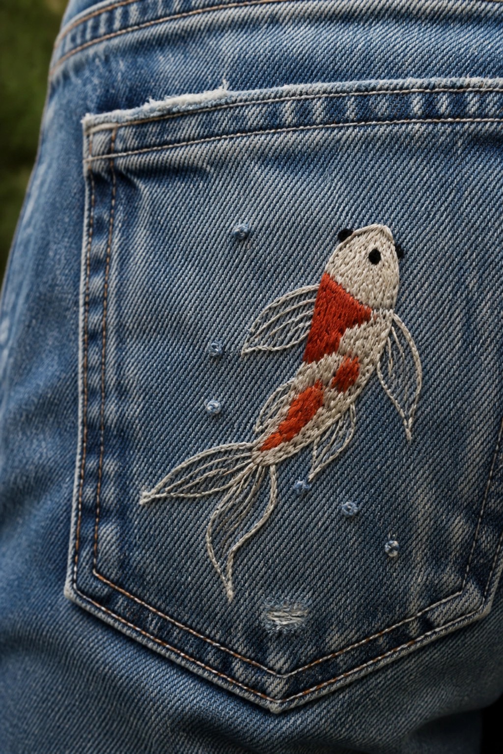Blue denim jeans pocket with embroidered white and orange koi fish and bubbles