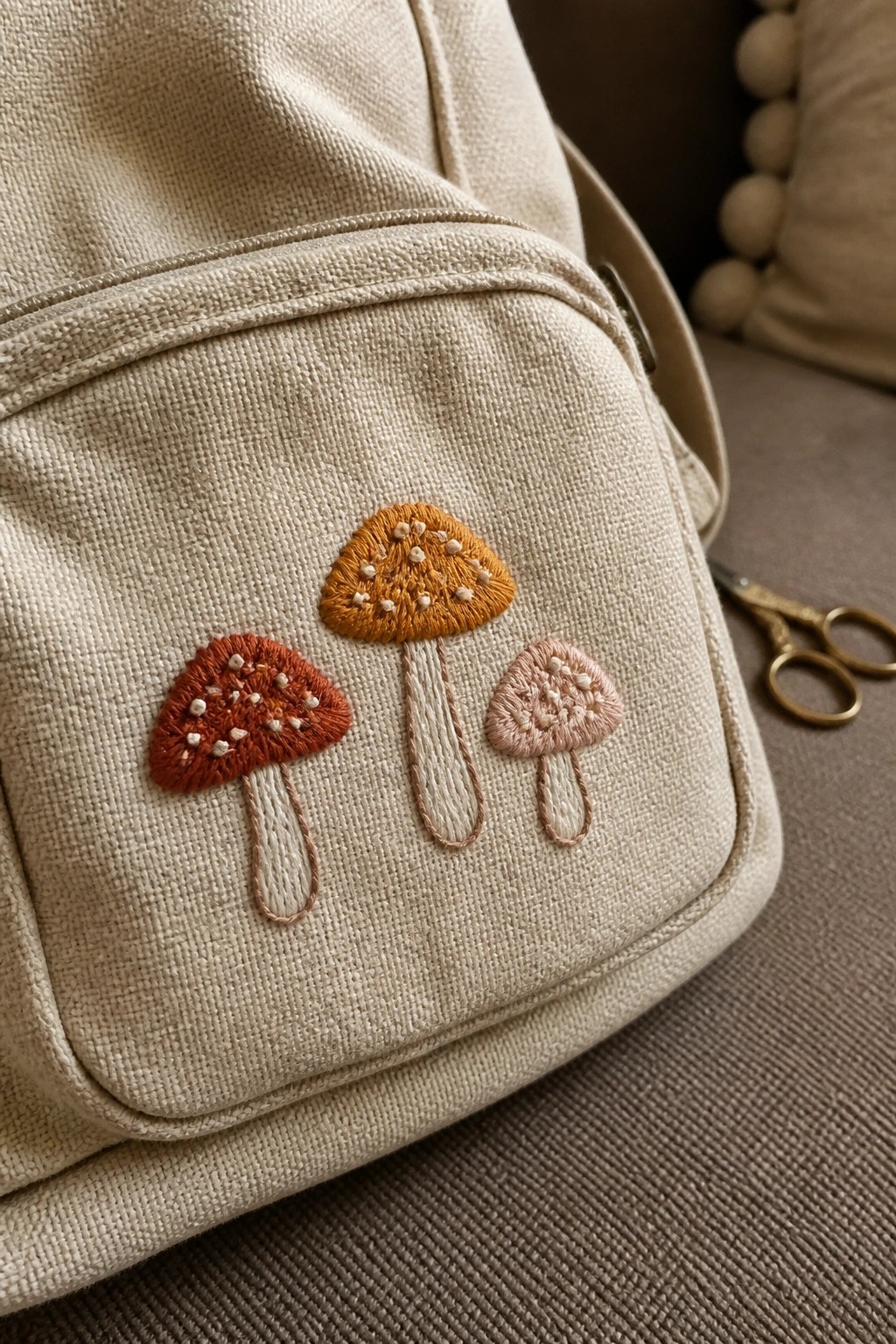 Beige canvas bag with hand-embroidered mushrooms in rust, orange, and pink.