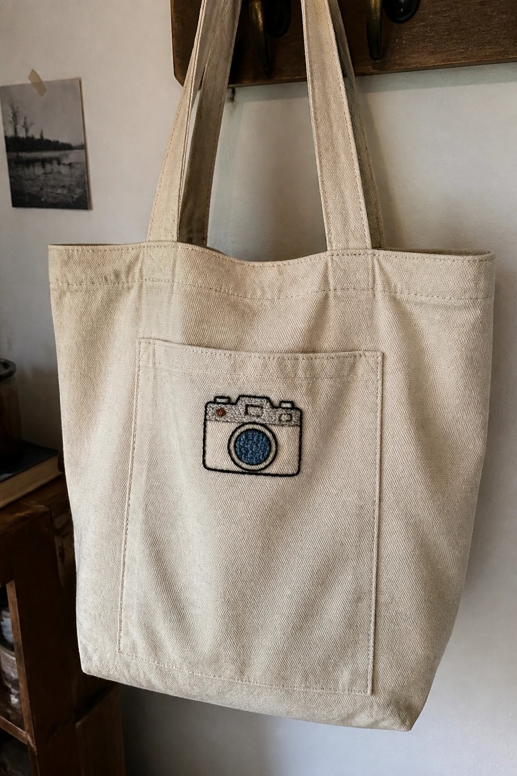 A beige canvas tote bag with a small camera embroidery centered on the front pocket.