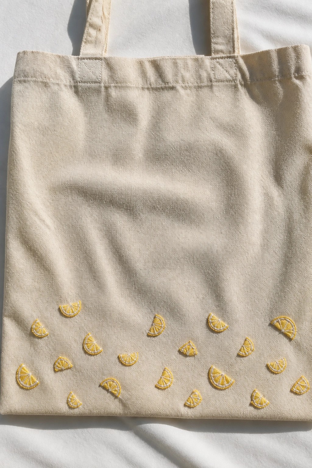 A beige canvas tote bag with multiple small yellow embroidered lemon slices scattered across the lower half.
