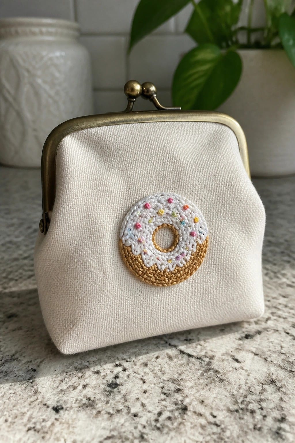 White fabric coin purse with embroidered donut and brass clasp on marble.