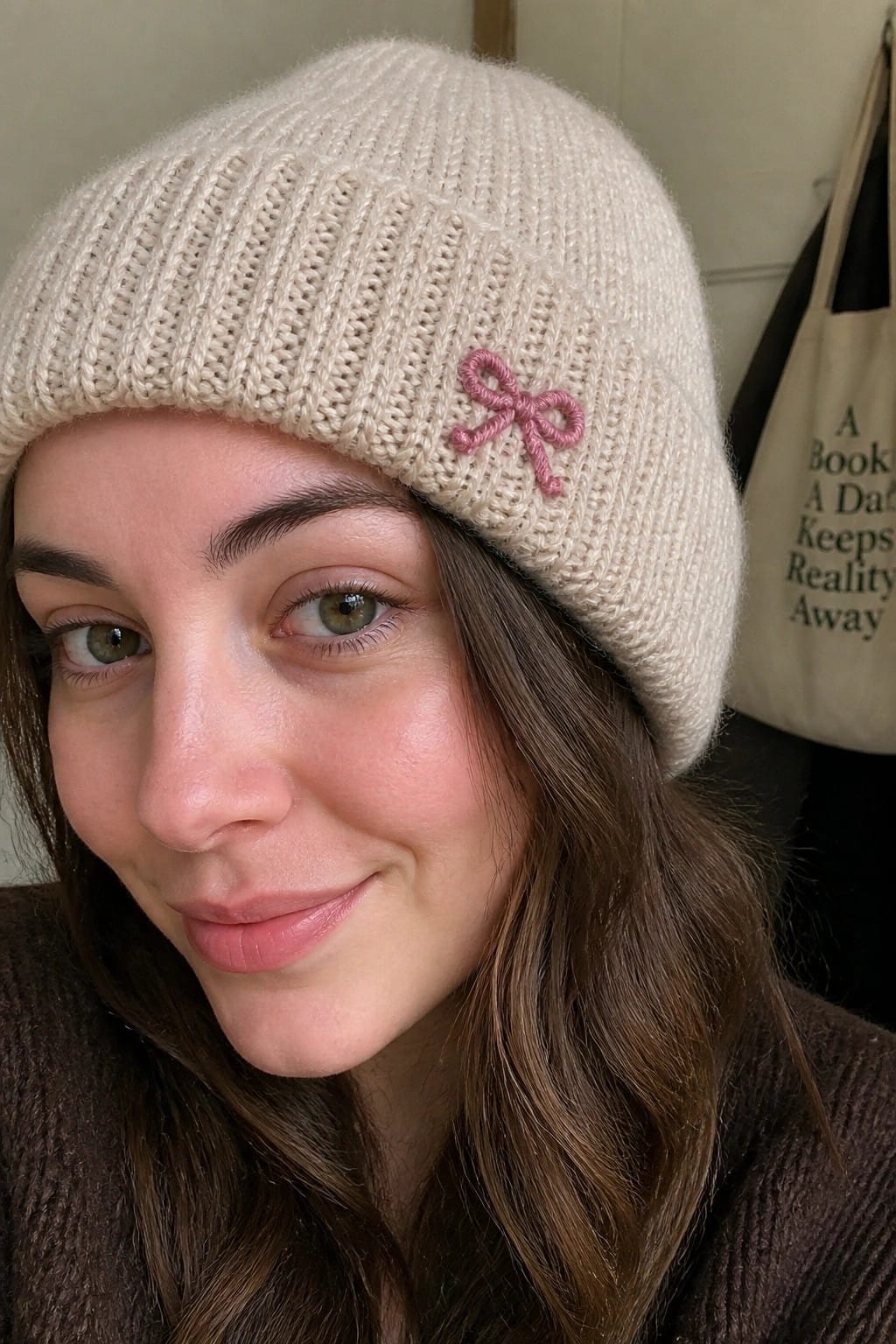 A woman wearing a cream knit beanie with a small pink embroidered bow on the side.