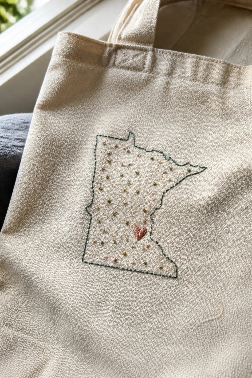 Embroidered Minnesota outline with colorful dots and pink heart on beige tote bag.