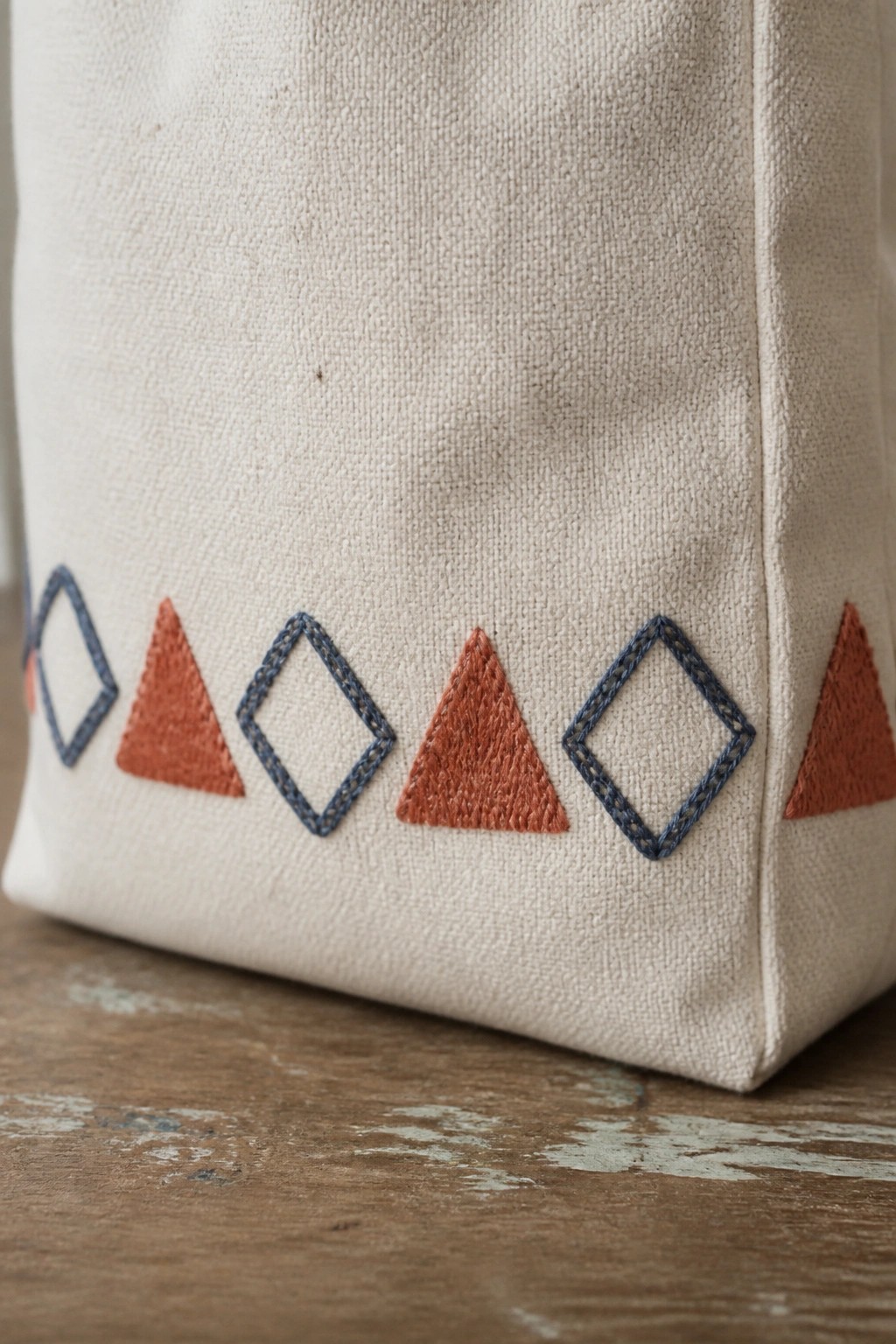 Beige canvas tote embroidered with terracotta triangles and blue diamonds on wood