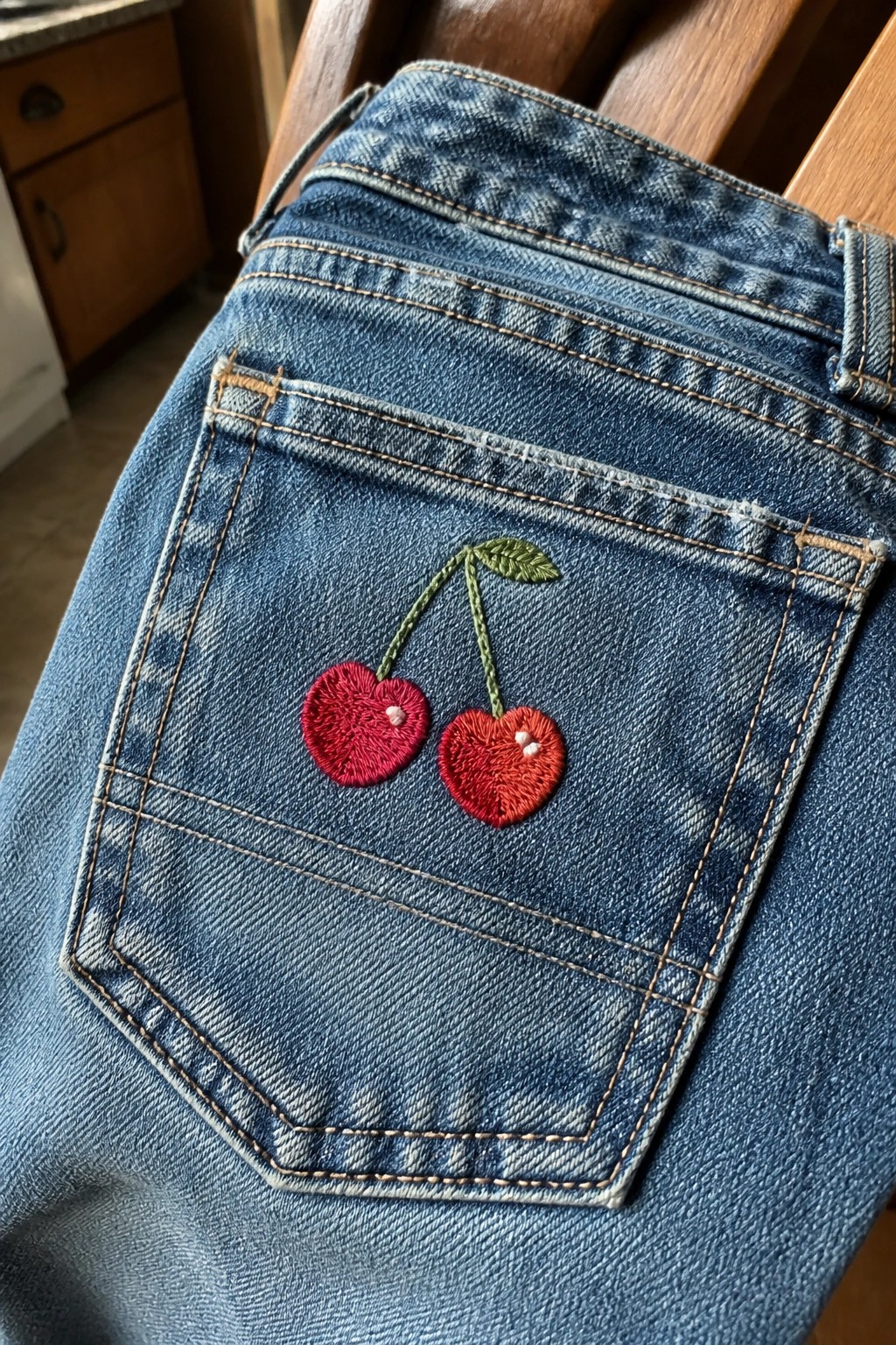 Blue denim jeans back pocket with two embroidered red cherries and green stems.