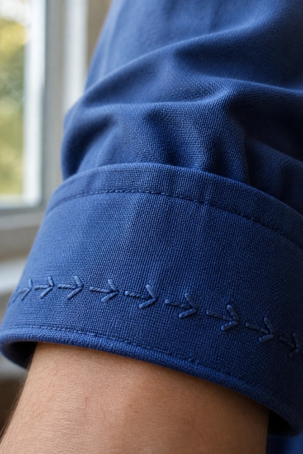 Close-up of rolled blue shirt cuff with dark arrow-shaped embroidery on hem.