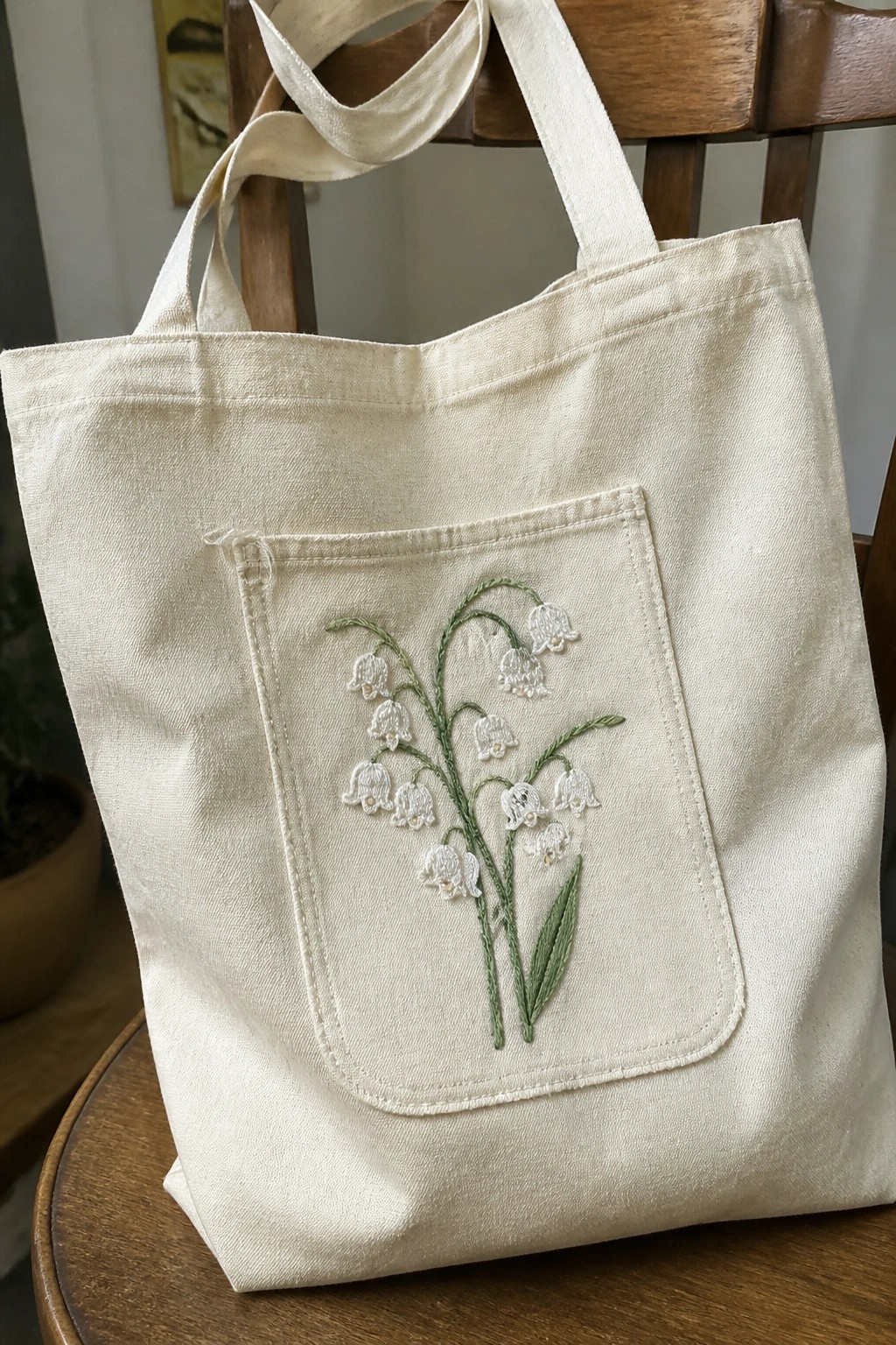 Cream canvas tote bag with embroidered lily of the valley on front pocket
