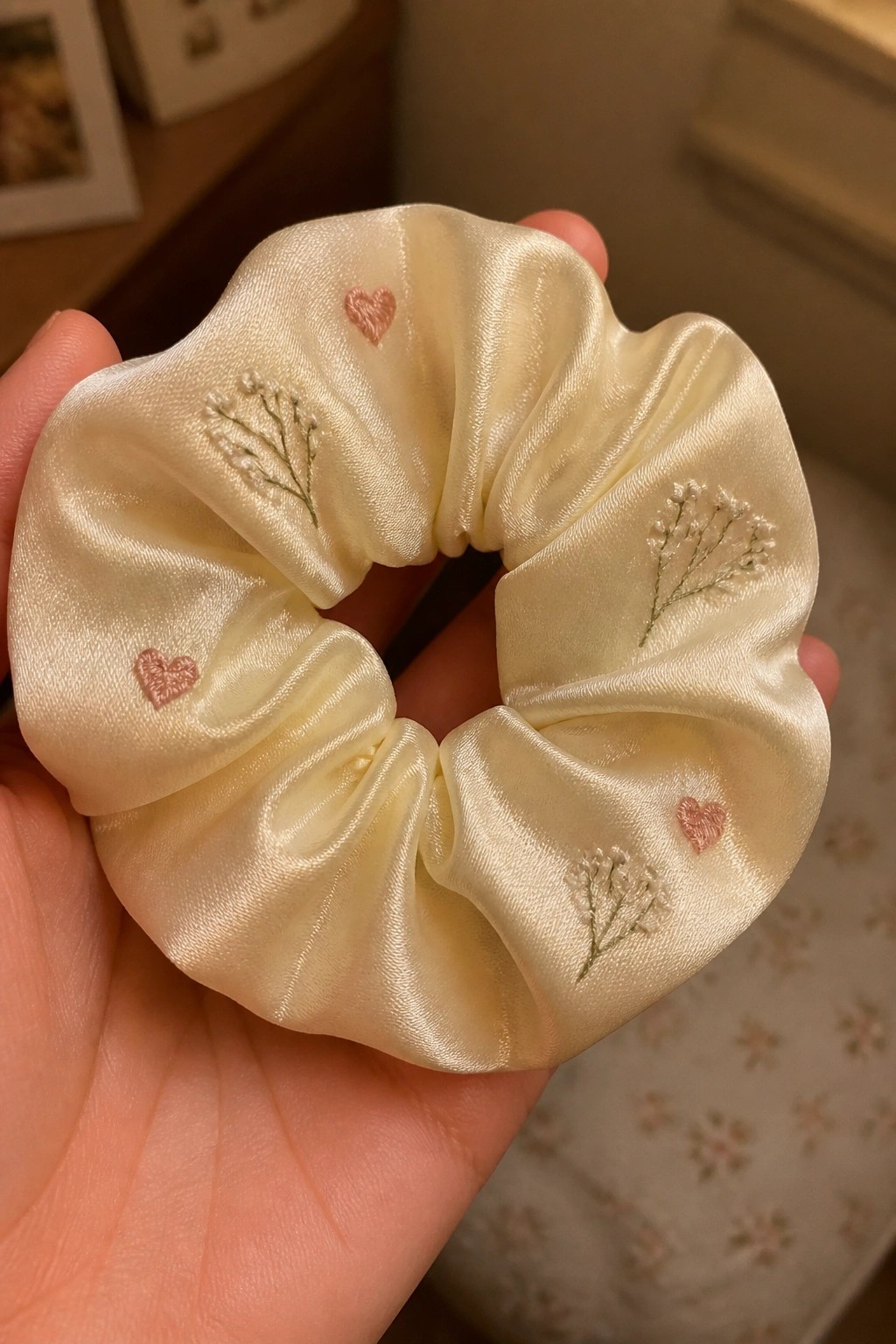 Hand holding cream satin scrunchie with pink hearts and green floral embroidery