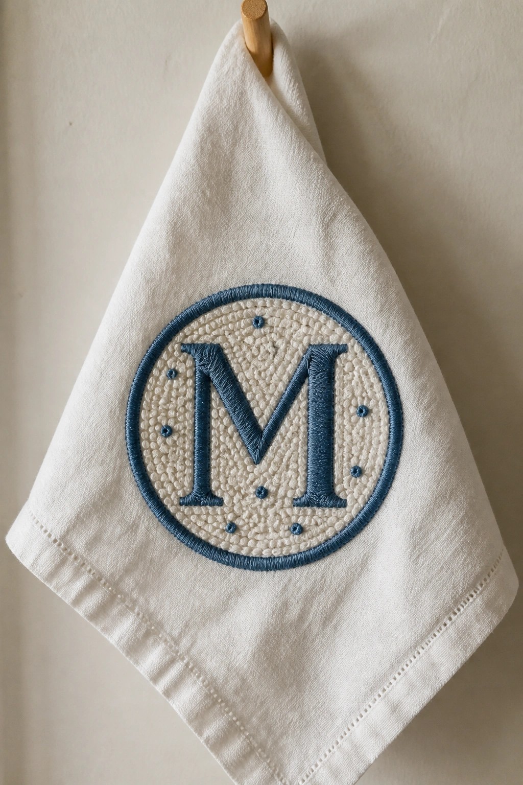 White towel with blue embroidered monogram M hanging from wooden peg