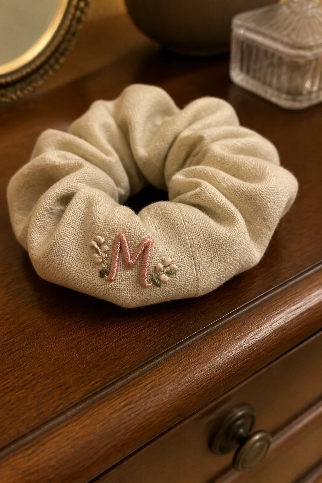 Beige linen scrunchie with pink embroidered M and florals on wooden dresser