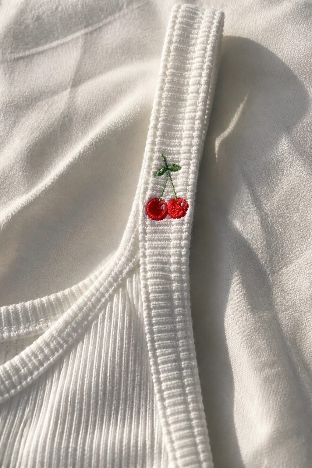 White ribbed tank top strap featuring embroidered red cherries with green stems