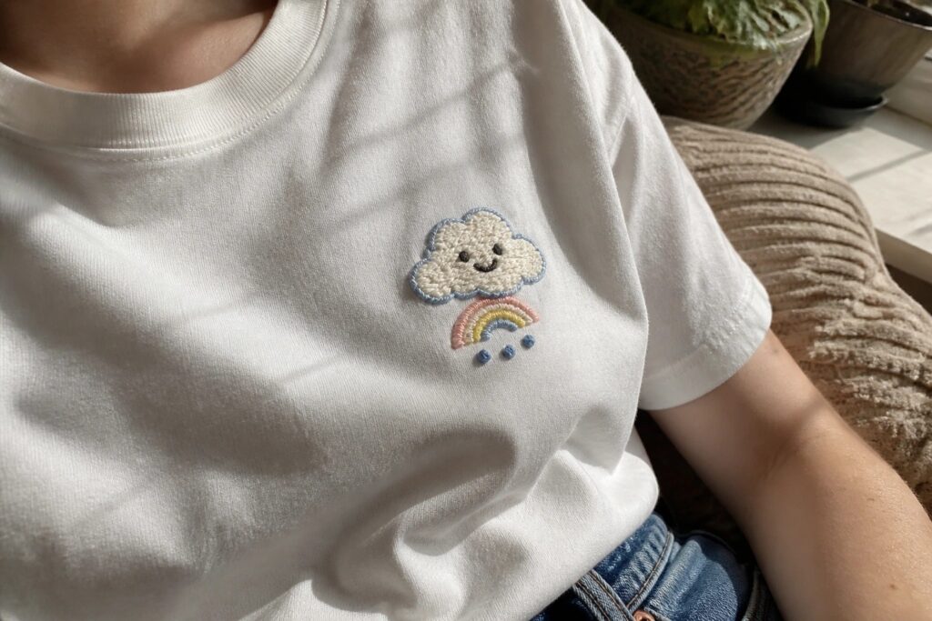 17 Trendy Cute Shirt Embroidery Ideas to Refresh Plain Everyday Basics White t-shirt with embroidered smiling cloud, rainbow, and blue raindrops